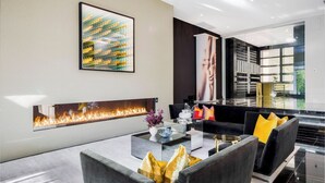 A modern living room with a fireplace, a large abstract painting, and a seating area with a glass coffee table. - London Dream (West Hollywood)