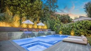 Piscina com borda de pedra, dois guarda-sóis e área com bancos.