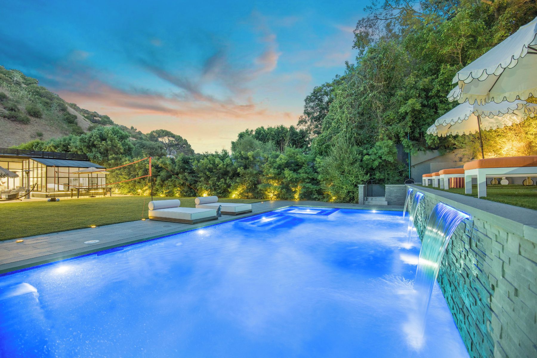 A swimming pool with a waterfall feature, surrounded by a deck with seating and a covered area.