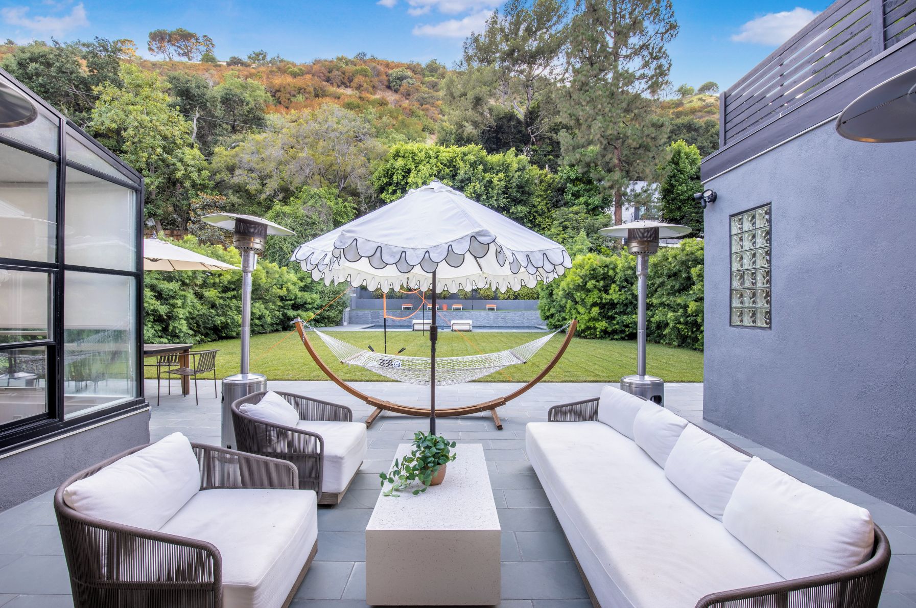 An outdoor seating area with wicker sofas, a central table with a plant, and a hammock.