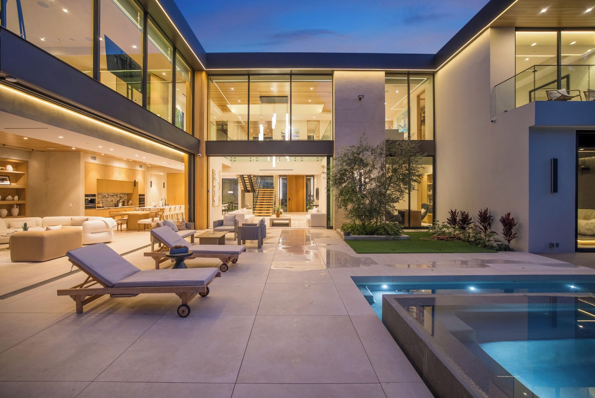 A modern house with a swimming pool, outdoor seating, and a well-lit interior.