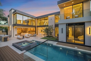 Ein modernes Haus mit Schwimmbad, Sitzgelegenheiten im Freien und einer großen Glasfassade.