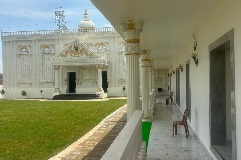 Un bâtiment à la façade blanche, doté d’une entrée centrale avec des marches et d’une allée couverte agrémentée de chaises.