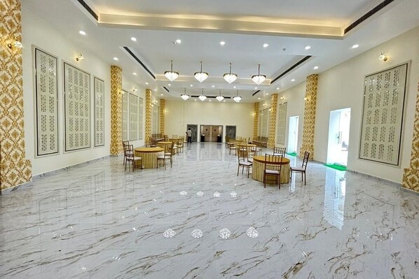 A spacious hall with marble flooring, multiple tables and chairs, and decorative wall panels.