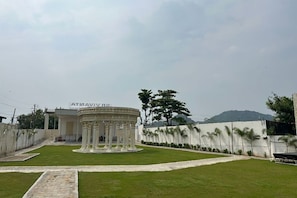 A circular structure with columns, a paved area, and a white building with a sign in the background.