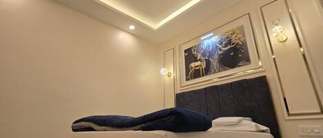 A hotel room with a bed, a ceiling light, a wall-mounted picture, and a nightstand.