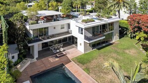 Una casa moderna de dos pisos con piscina en la azotea, grandes ventanales y un jardín cuidado.