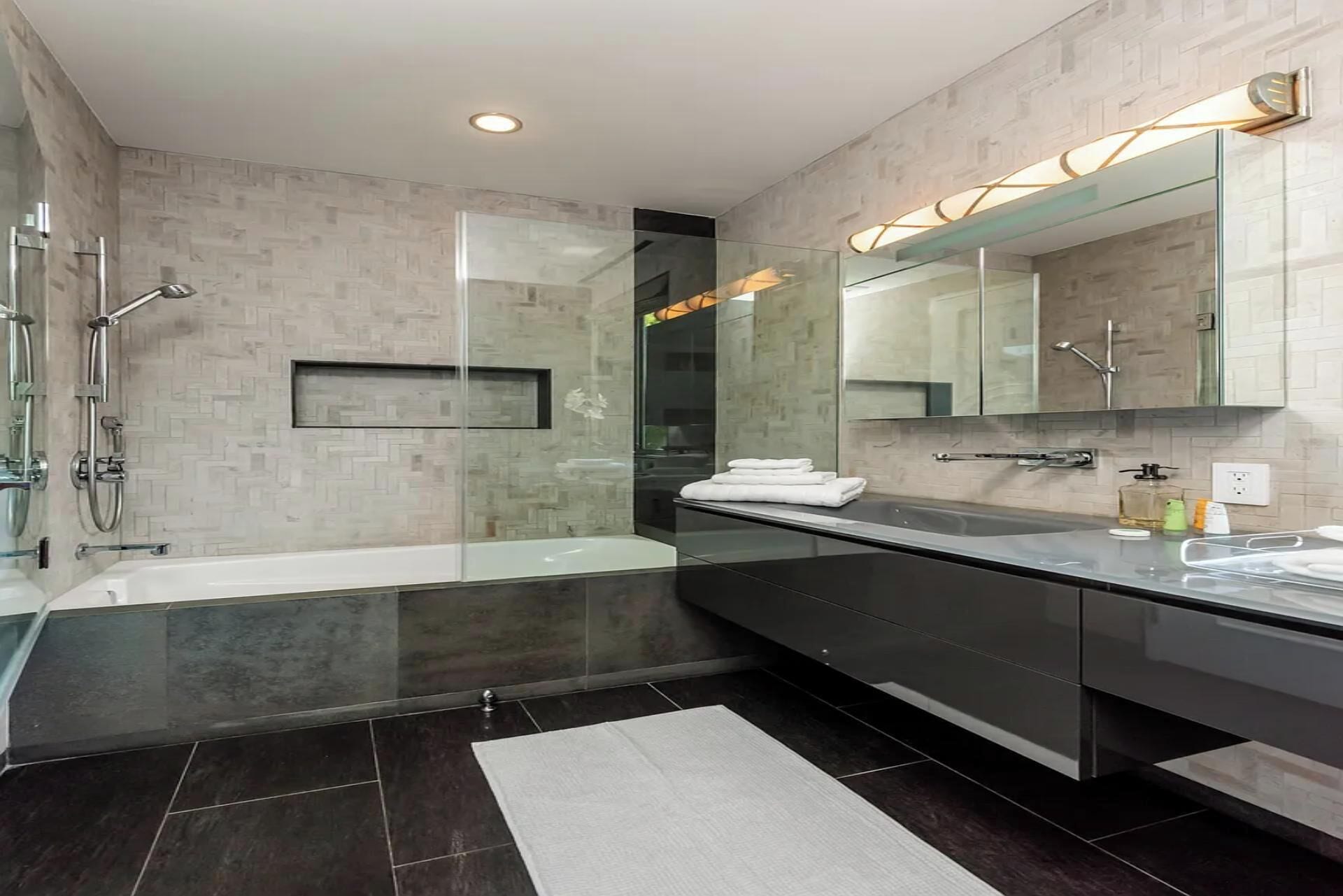 Une salle de bain moderne avec une douche à parois de verre, un grand miroir et un sol recouvert de carreaux foncés.