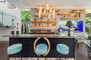 A modern kitchen with a central island, bar stools, a hanging light fixture, and a fish tank. - Alta Royale (West Hollywood)
