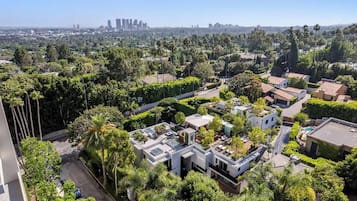 Vista aérea de um bairro residencial com casas modernas, vegetação exuberante e um horizonte urbano distante.