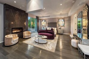 A spacious living room with a fireplace, a large window, and a chandelier. - Alta Royale (West Hollywood)