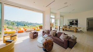 A spacious living room with a large window overlooking a lush landscape. - Zen Estate (Beverly Hills)
