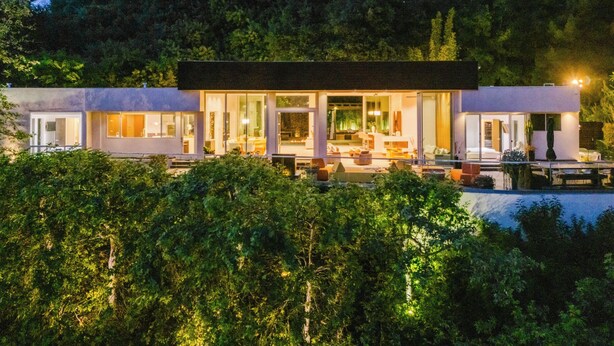 A modern, multi-story house with large glass windows, a pool, and lush greenery surrounding it. - Zen Estate (Beverly Hills)