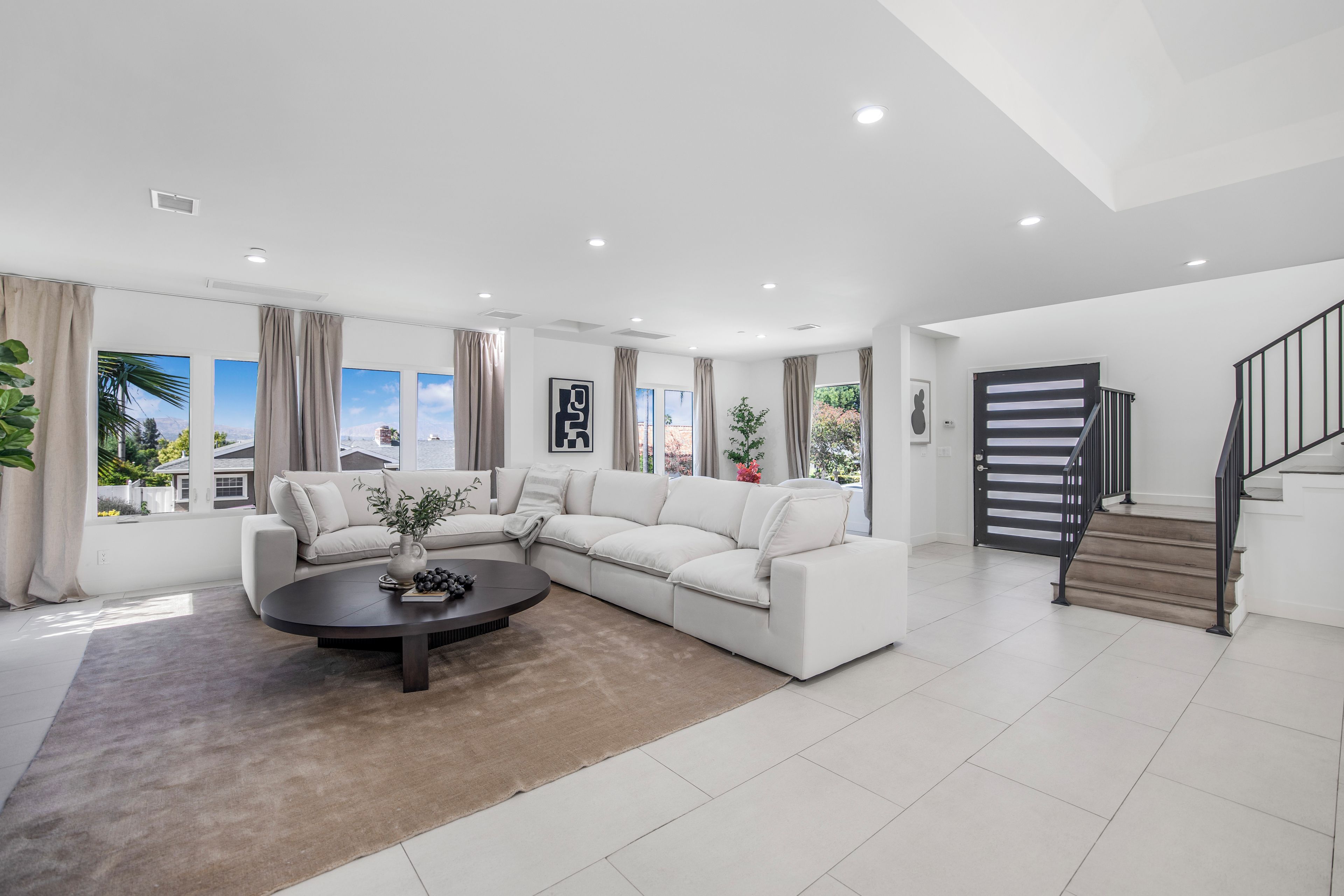 A modern living room with a white sofa, a round coffee table, and a staircase with a black railing.