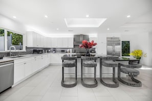 A modern kitchen with white cabinets, a central island, and bar stools. - Rancho Haven (Tarzana)
