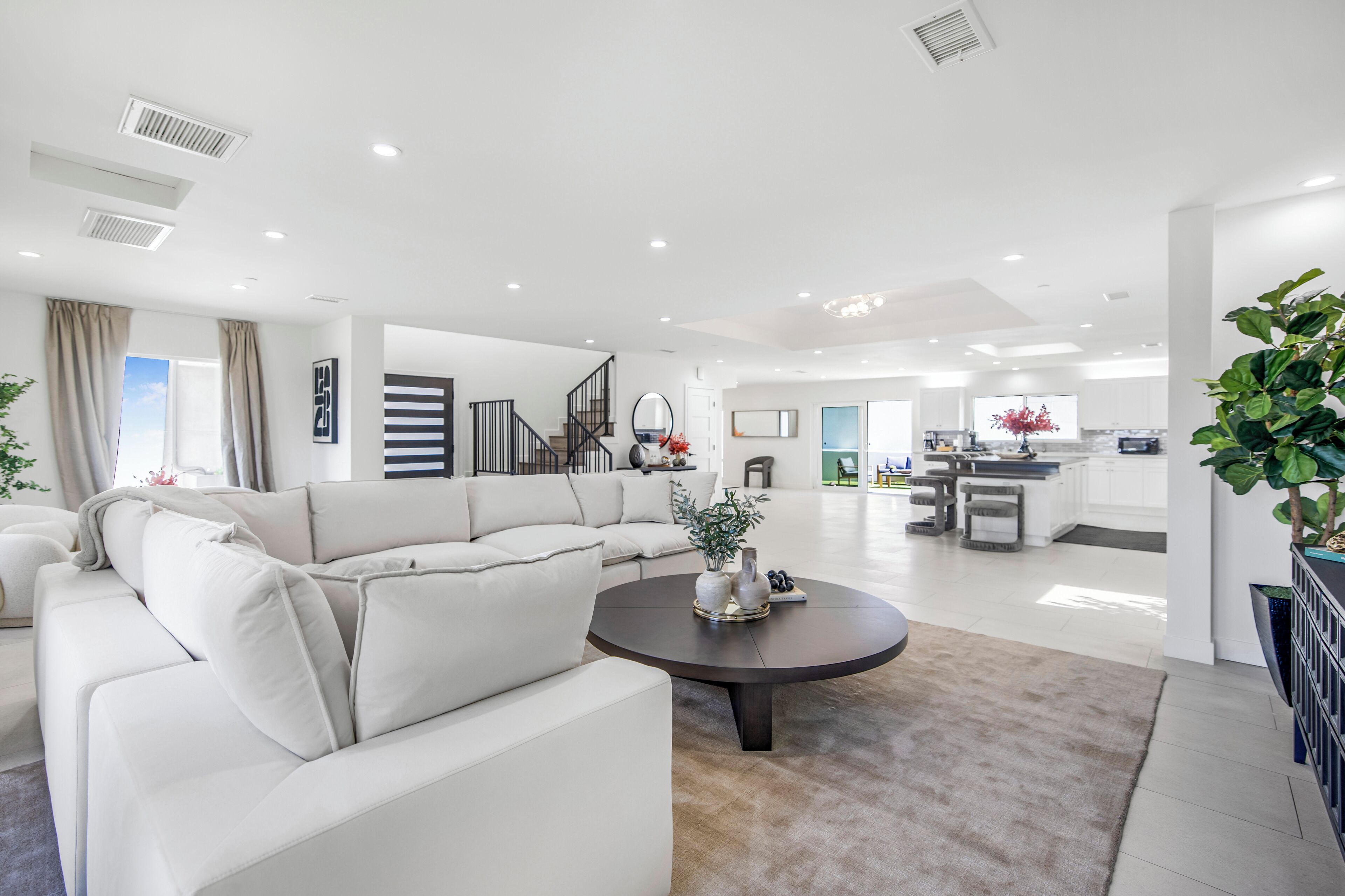 A spacious living room with a large white sectional sofa, a round coffee table, and a kitchen in the background.