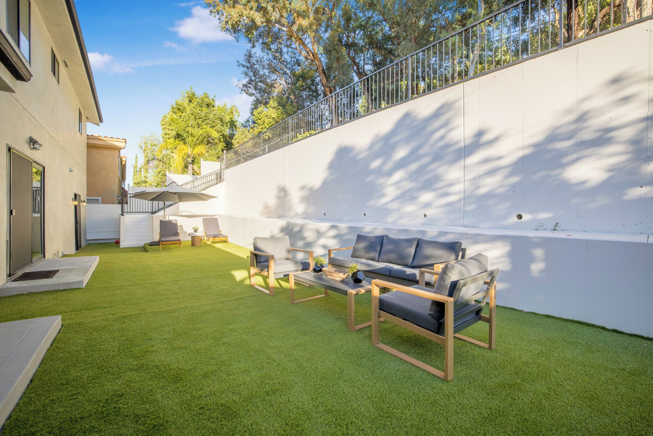Un patio exterior moderno con un conjunto de sofás, una mesa de centro y una mesita con una planta.