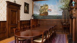 A formal dining room with a large wooden table, chairs, a patterned rug, a maritime mural, and traditional decor. - Hotel Keizershof (Amsterdam)