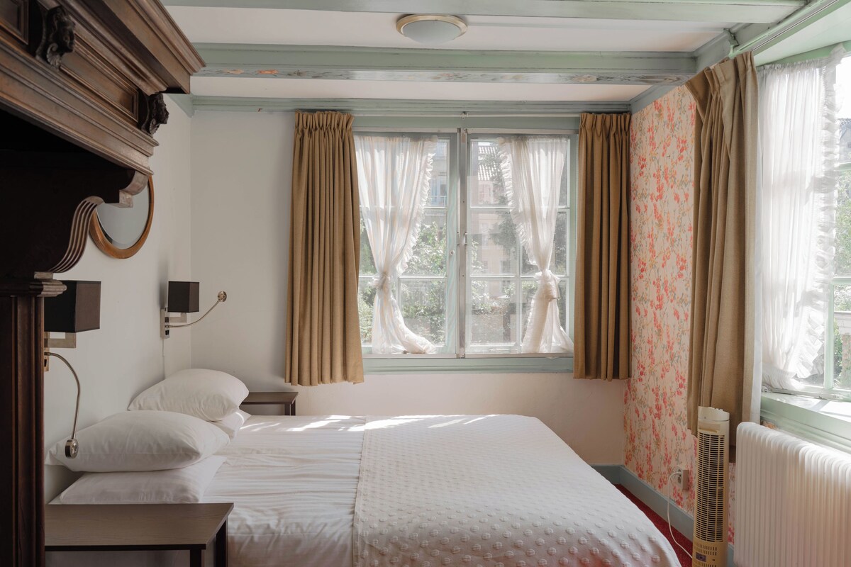 A bedroom with a large bed, a bedside table, a mirror, and a window with curtains.