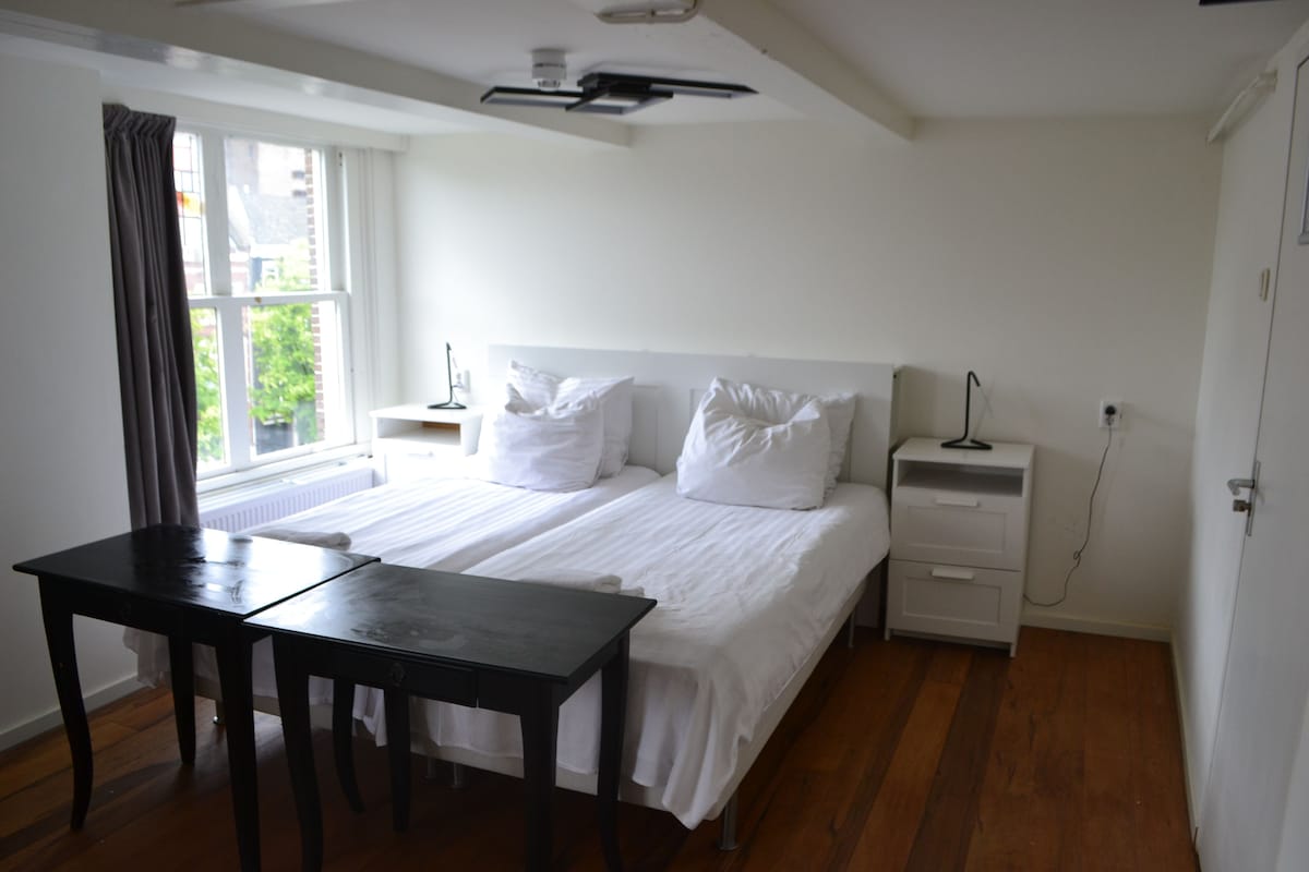 A bedroom with a bed, bedside tables, a desk, and a window.