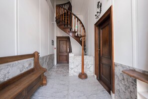 A marble-floored hallway with a wooden bench, a wooden door, and a spiral staircase. - Hotel Keizershof (Amsterdam)