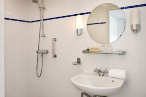 Un baño con ducha, lavamanos, espejo y estante con artículos de aseo.