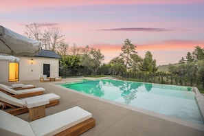 A modern outdoor pool area with lounge chairs and a small building with a door and windows. - Lechusa Estate (Malibu)