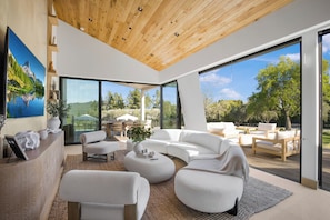 A modern living room with a large white sectional sofa, a round coffee table, and a wooden ceiling. - Lechusa Estate (Malibu)