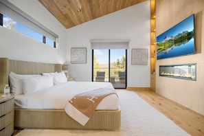 A modern bedroom with a large bed, a fireplace, a TV, and a balcony with a view. - Lechusa Estate (Malibu)
