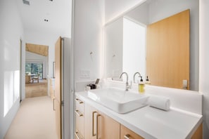 A modern bathroom with a large sink, mirror, and wooden cabinets. - Lechusa Estate (Malibu)