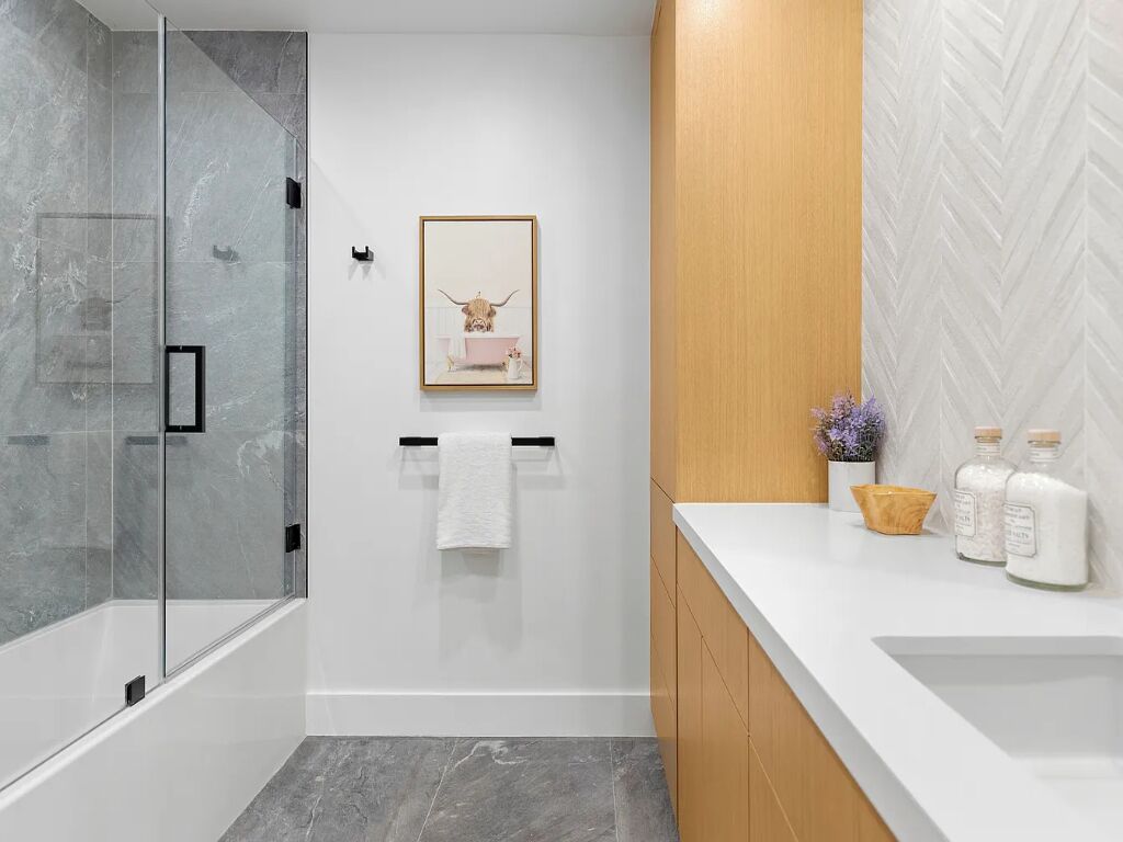 A modern bathroom with a glass shower enclosure, a wooden vanity, and a herringbone-patterned wall.