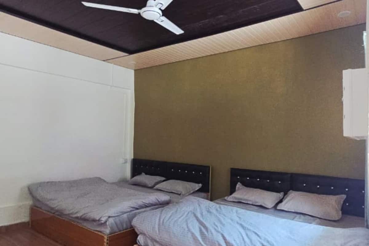A room with two beds, a ceiling fan, wooden flooring, and a plain wall.