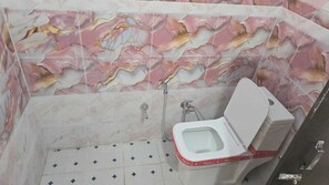 A bathroom with a marble wall, a toilet, and a shower.