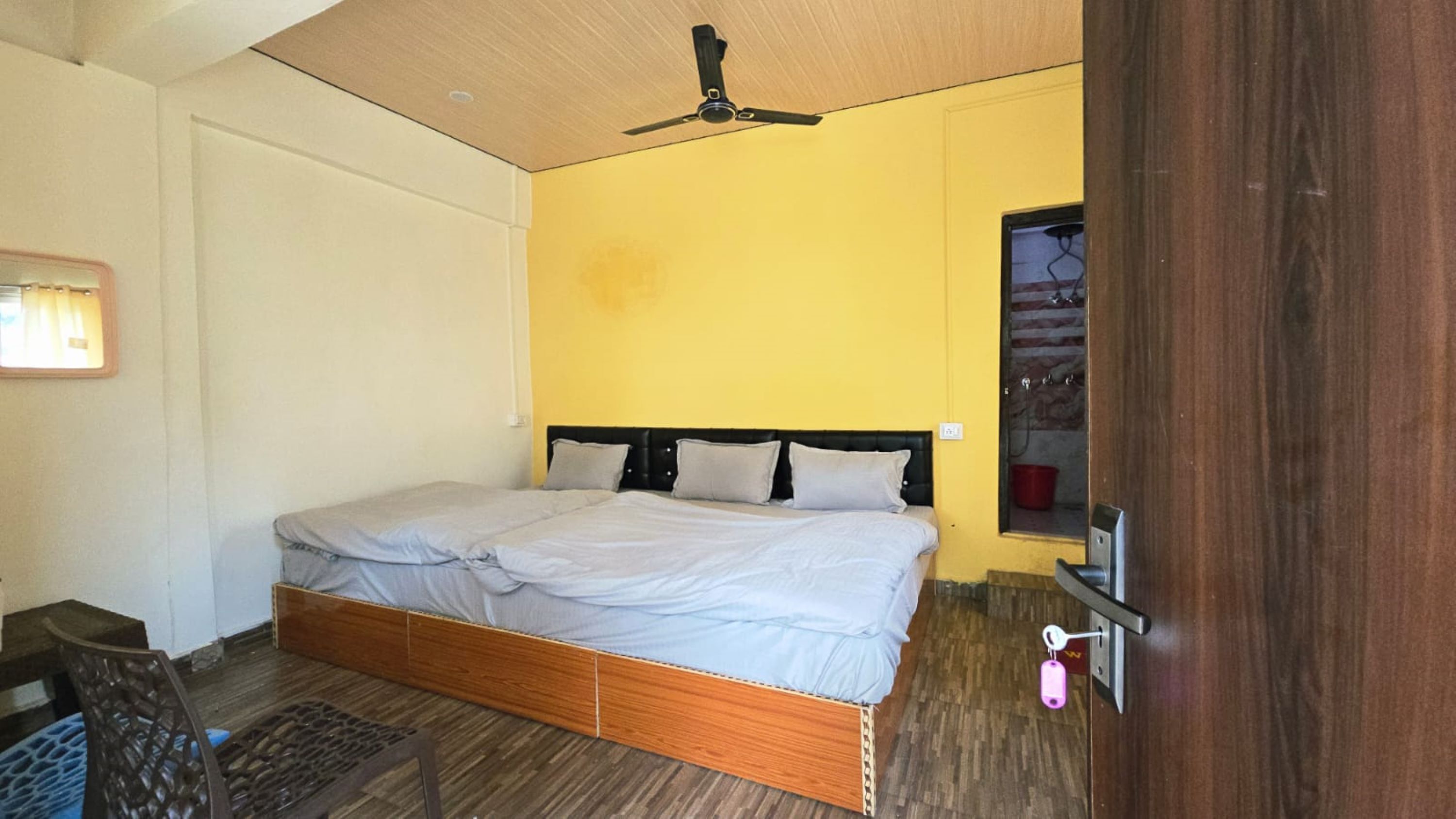 Une chambre à coucher avec un lit, un ventilateur de plafond, un plancher en bois et un petit bureau.