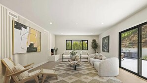 A modern living room with a fireplace, a sofa, a chair, and a large window offering a view of the outdoors. - The Dona Modern (Studio City)