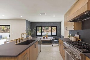 Una cocina moderna con una isla central, encimeras oscuras, armarios de madera y un amplio ventanal con vistas al exterior.