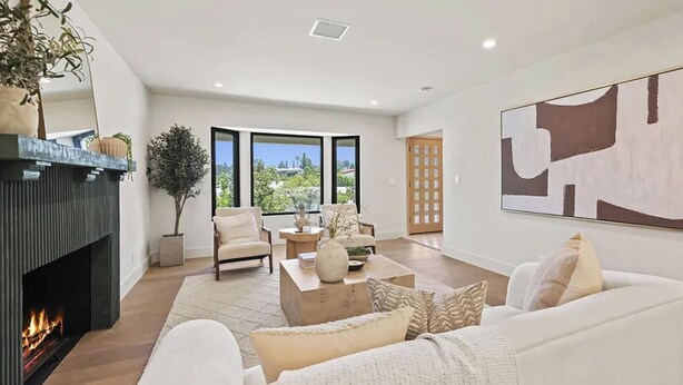 A modern living room with a fireplace, comfortable seating, a large window, and a view of the outdoors. - The Dona Modern (Studio City)