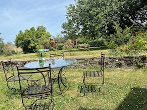 Una mesa redonda de cristal con sillas de metal, rodeada por un muro de piedra y abundante vegetación.