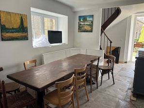 Un comedor con una mesa larga y sillas, una ventana con un cuadro, un radiador y una escalera.