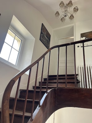 Eine Holztreppe mit Handlauf, einer Chandelüster und einem Gemälde an der Wand.