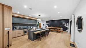 A modern kitchen with a central island, wooden flooring, and a dining area with a bench. - Farley Court (Studio City)