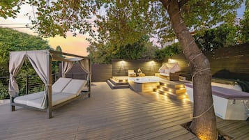 Um deck de madeira com cama de dossel, hidromassagem e área de estar com um tronco de árvore incorporado ao design.
