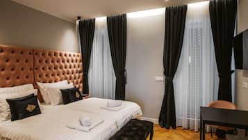 Habitación de hotel con tablero de cabecera capitonado, cama con ropa de cama blanca, banca negra, escritorio y cortinas translúcidas.
