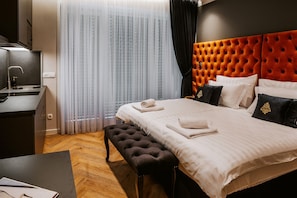 Ein Hotelzimmer mit Bett, einer Sitzbank, einem Schreibtisch und einem Fenster mit Vorhängen.