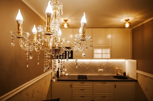 Un candelabro con múltiples lámparas y decoraciones de cristal en una habitación con zona de cocina.