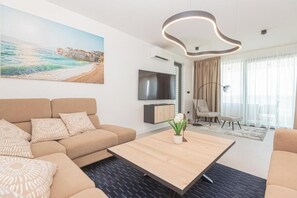 Ein modernes Wohnzimmer mit einer Couch, einem Couchtisch, einem Fernseher und einem Gemälde, das eine Strandansicht zeigt.
