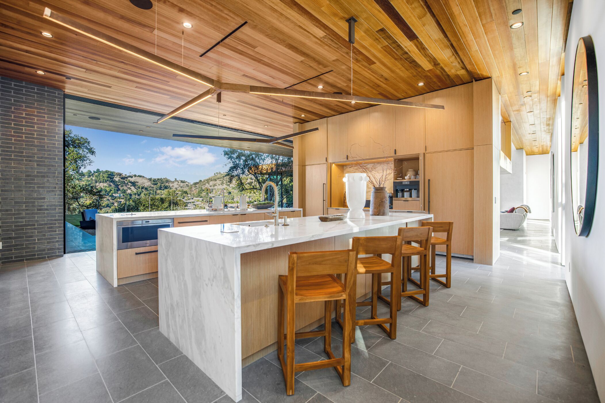 Cozinha moderna com uma ilha grande, cadeiras de madeira e vista para uma paisagem montanhosa.