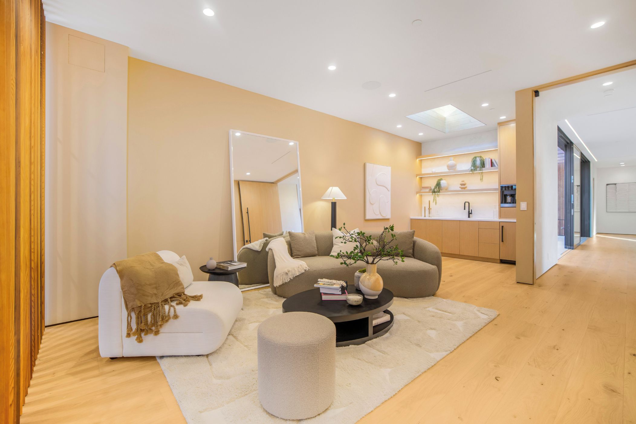 Una sala de estar moderna con un sofá, una mesa de centro y un reposapiés, una cocina al fondo y un espejo grande.