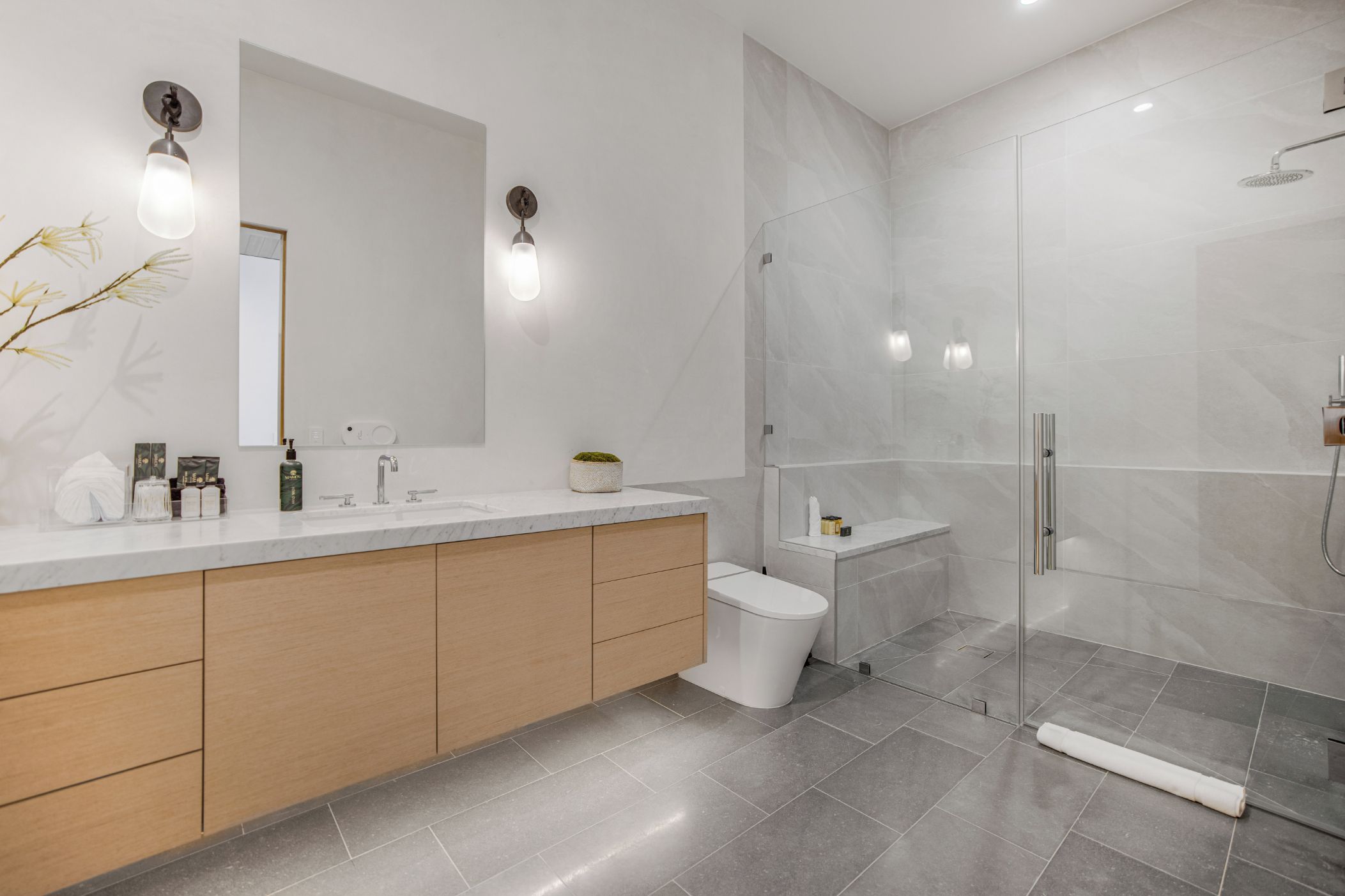 Un baño moderno con tocador de mármol, cabina de ducha de vidrio y un espejo grande.