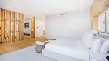 A modern bedroom with a large bed, a wooden partition, and a TV in the background.